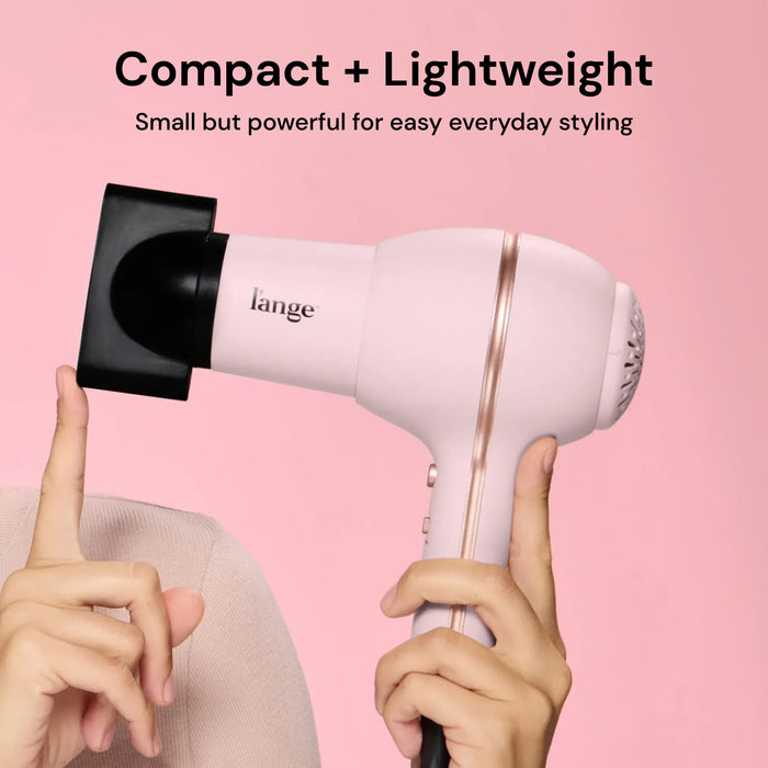Hands holding L'ange Hot Stuff blush hair dryer with concentrator on pink background. "Compact + Lightweight – Small but powerful for easy everyday styling"