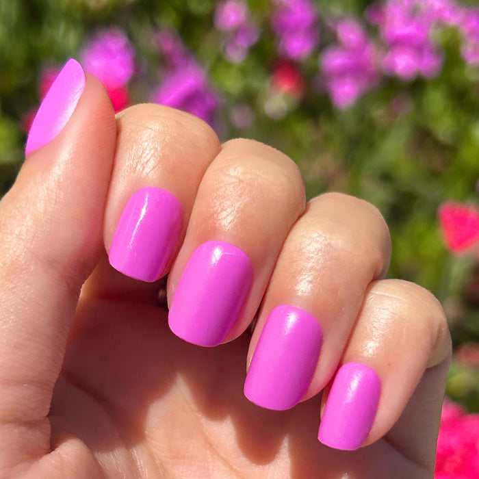 Jam, Please - Press-On | Extra Short | Squoval showing hand with bright soft magenta false nails outdoors by flowers