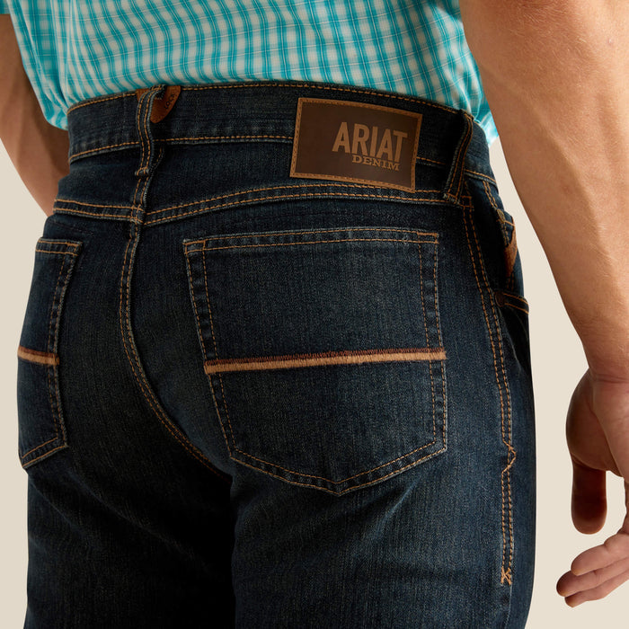 Men's Ariat M4 dark wash Pro series relaxed fit boot cut jean. Rear view showing back pocket and side stitching details along with a Ariat Denim patch.
