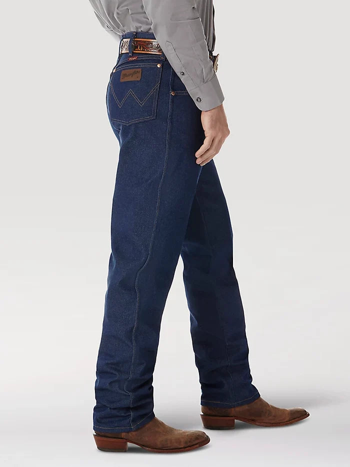A man wearing Wrangler® Cowboy Cut® relaxed fit rigid blue jeans with western shirt, belt, and boots. Side view shows brown neolite patch on right back pocket.