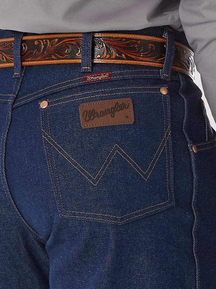 Closeup of back right back pocket of a man wearing Wrangler® Cowboy Cut® relaxed fit rigid blue jeans with western shirt and belt. Pocket has copper rivets on top corners, "W" stitched on pocket, and neolite brown logo patch.