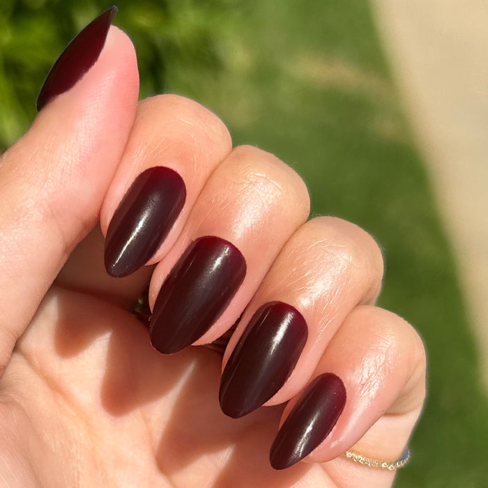 Obsessed - Press-On | Medium | Almond showing hand with dark ruby almond press-on manicure outdoors in sunlight