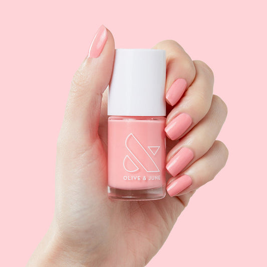 Hand with glossy nails painted in Pen Pal polish by Olive and June holding matching coral pink bottle