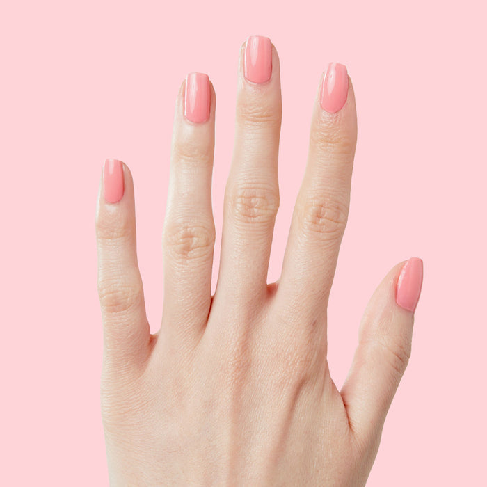 Hand with nails coated in Pen Pal bright bubblegum pink long-lasting polish by Olive and June on pale pink background