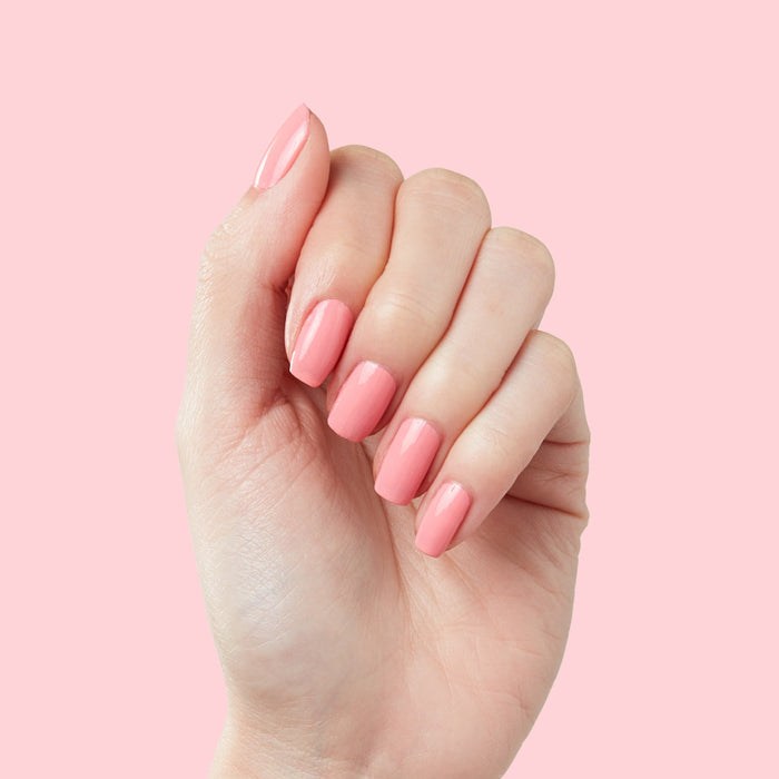 Hand showing medium-length nails polished in bright bubblegum pink Pen Pal by Olive and June on pale pink background