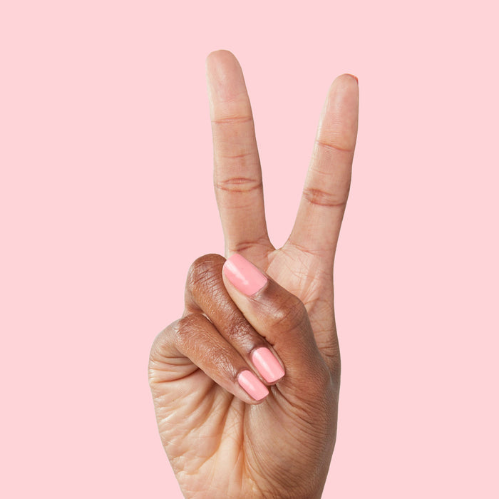 Hand showing medium-length nails polished in Pen Pal bright bubblegum pink by Olive and June on pale pink background