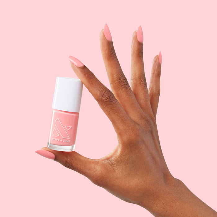 Hand with medium-length nails painted in Pen Pal bright bubblegum pink holding matching Olive and June polish bottle on pink background