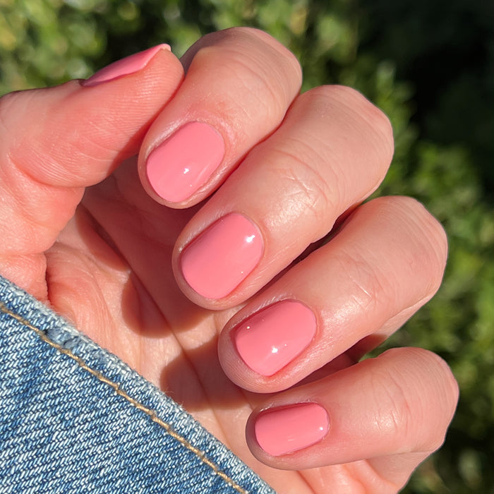 Hand with short nails painted in Pen Pal bubblegum pink long-lasting gel polish by Olive and June outdoors