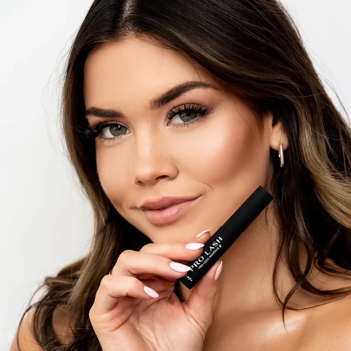 Lash sealer held by woman with voluminous eyelash extensions and flawless makeup for long-lasting lash hold.