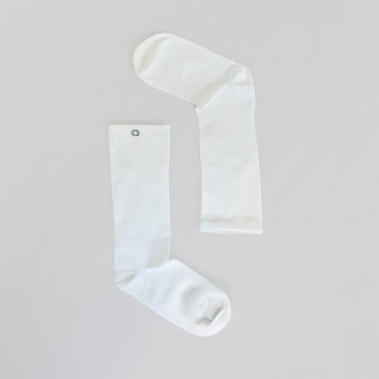 Two plain white socks laid flat on a light surface, positioned to form an angled shape resembling an upside-down letter L. One sock has a small gray circular emblem near the top.