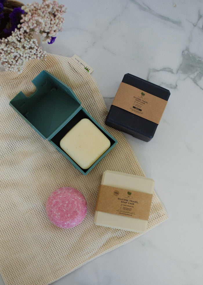Three bars of soap on a textured surface with a pink loofah and a green soap dish.