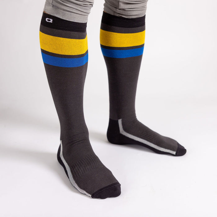 A person wearing knee-high dark gray socks with yellow and blue stripes near the top, standing on a white background. The person is also wearing light gray leggings.