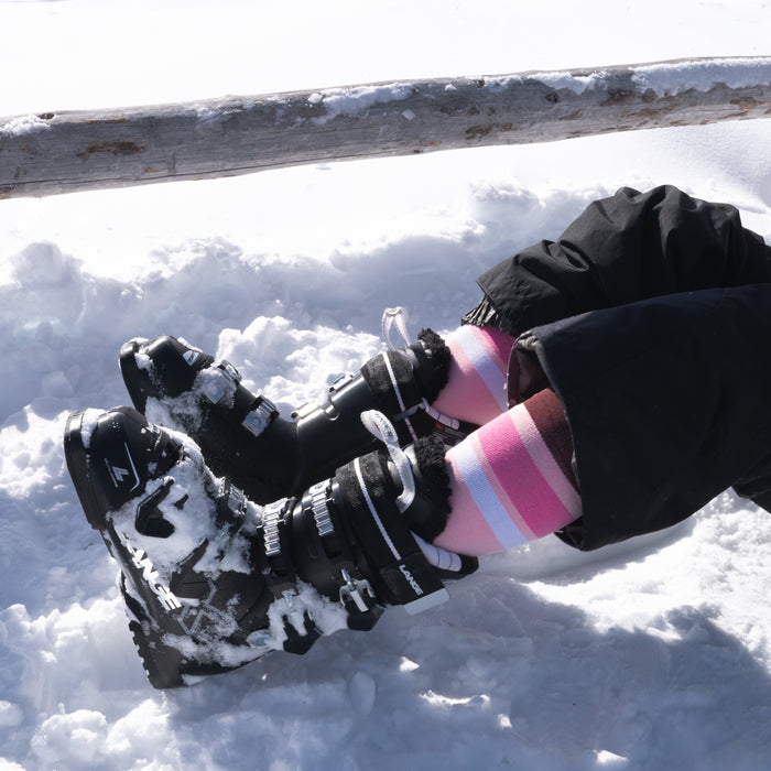 A person wearing ski boots and pink socks sitting in snow.