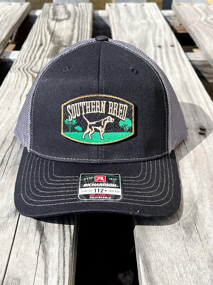 A black and gray Southern Bred cap with a logo on the front, placed on a wooden surface.
