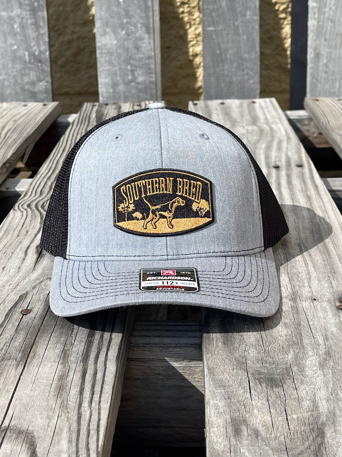 A heather grey Southern Bred baseball cap with a logo on the front and an adjustable snapback closure, placed on a wooden surface.