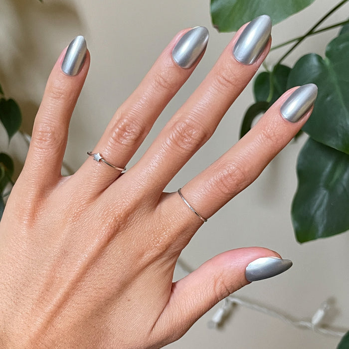 Hand with Steel Velvet - Press-On | Medium | Almond nails in sleek steely silver metallic finish with delicate silver rings and green leaves background