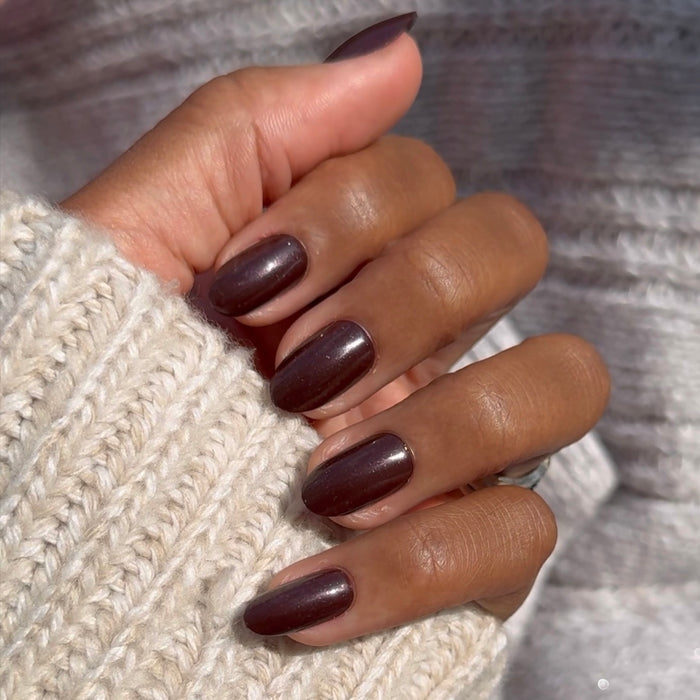 Hand with medium oval deep plum metallic shimmer nails wearing To Me, You Are Perfect - Press-On | Medium | Oval on cozy sweater background