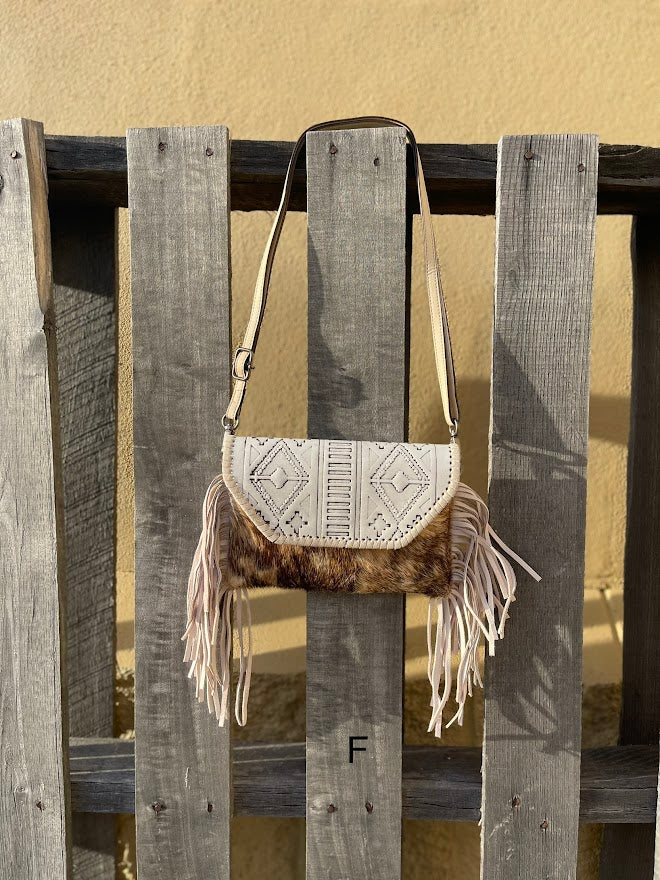 This cowhide and Beige leather bag features fringe sides and can be used as a wristlet or crossbody. It has a geometric print debossed flap with a whipstitch border.  Front View F
