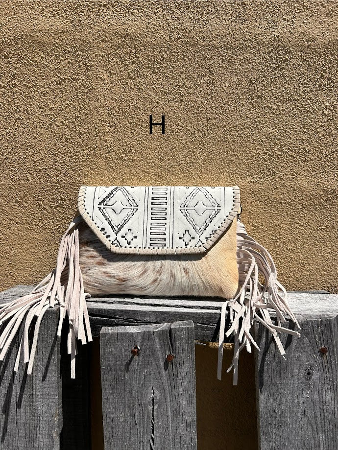 This cowhide and Beige leather bag features fringe sides and can be used as a wristlet or crossbody. It has a geometric print debossed flap with a whipstitch border.  Front View H