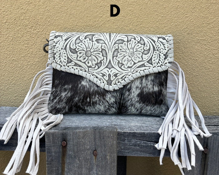 Clutch bag with white fringe and intricate design on a wooden surface against a beige wall.