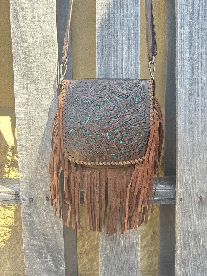 This Coffee Brown tooled leather crossbody bag has a turquoise inlay in the flap closure bordered with whip stitch. It has brown fringe, strap, and back. Front View