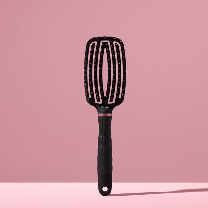 black L’ange vented paddle brush with nylon bristles standing upright on pink background