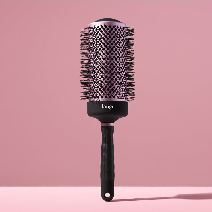 Black round brush for styling hair with a blow dryer against a blush background.
