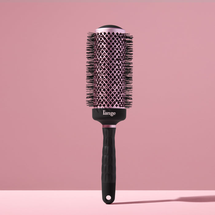 Black round brush for styling hair with a blow dryer against a blush background.